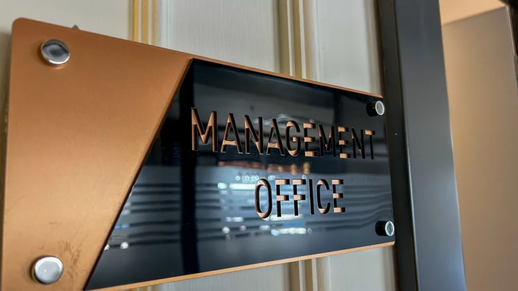 An indoor sign on an office wall that reads MANAGEMENT OFFICE in block stencil-looking letters.