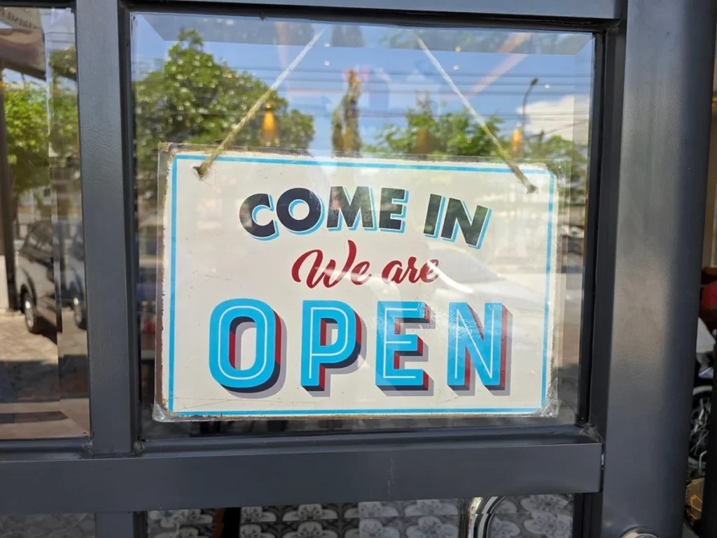An interior sign hanging in a cafe’s windowed door that reads 'COME IN We are OPEN.'
