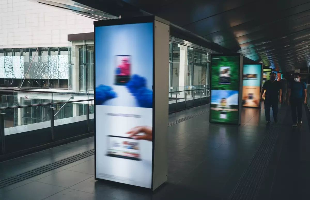 People walking in an urban area alongside digital signage kiosks.