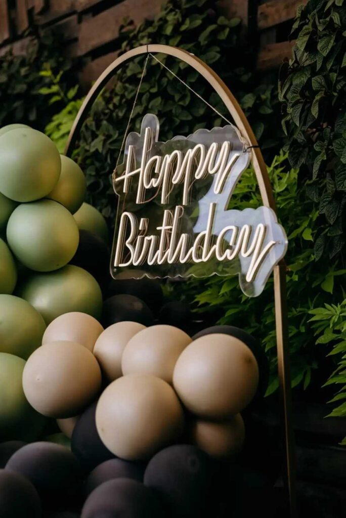 A neon-looking light-up Happy Birthday sign surrounded by balloons.