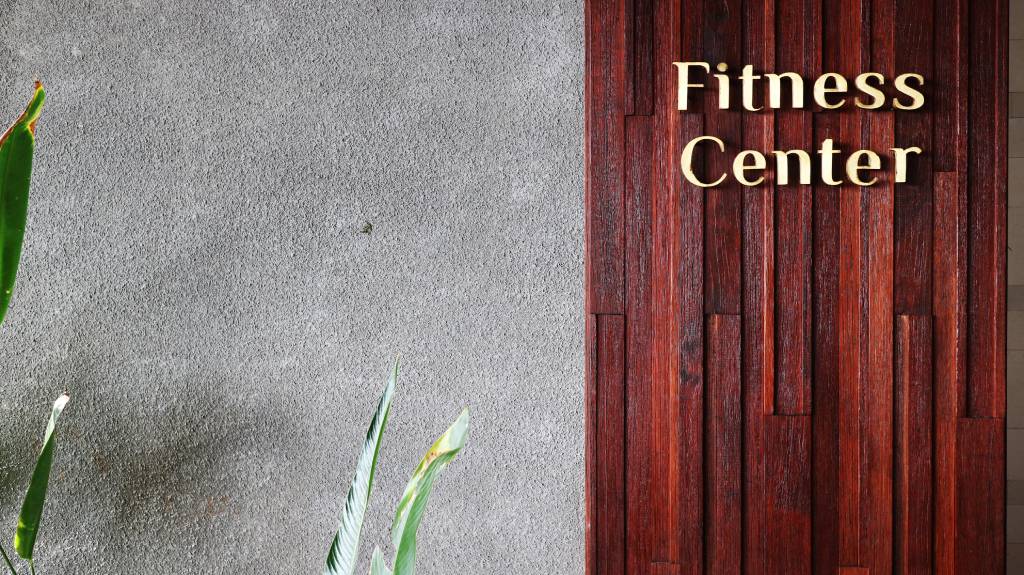Gold lettering for "Fitness Center" mounted on a rich dark wood panel next to a textured grey concrete wall.