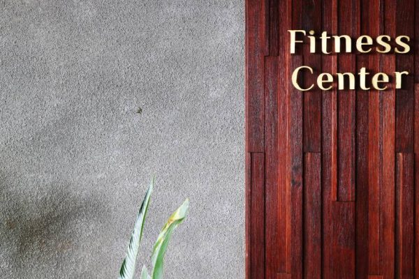 Gold lettering for "Fitness Center" mounted on a rich dark wood panel next to a textured grey concrete wall.