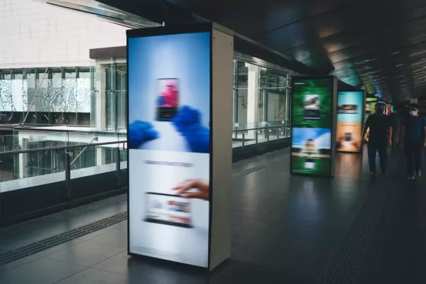 People walking in an urban area alongside digital signage kiosks.