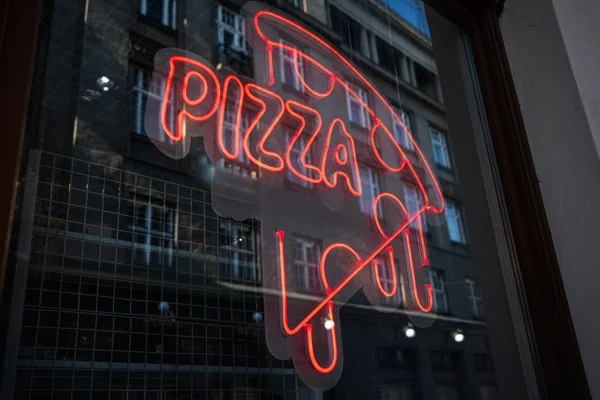Illuminated red neon pizza sign in a storefront window.