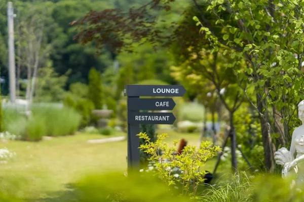 Outdoor signage with three wooden arrow shapes pointing in the same direction, reading LOUNGE, RESTAURANT, and CAFE.