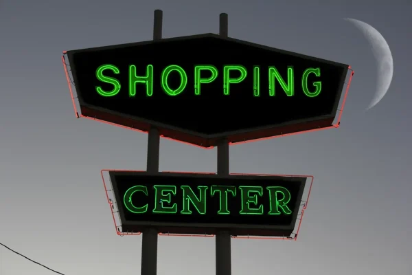 A tall pylon sign with lettering that reads SHOPPING CENTER in emerald green lights